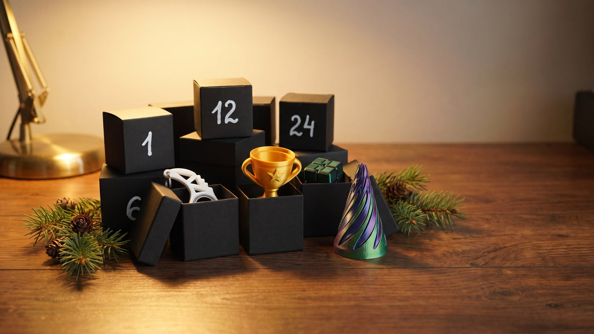 Small matte black gift boxes numbered 1, 6, 12 and 24 on a wooden desk, with a white karambit keychain spinner, a gold mini trophy, a black-green infinity cube and a spiral cone fidget among pine sprigs