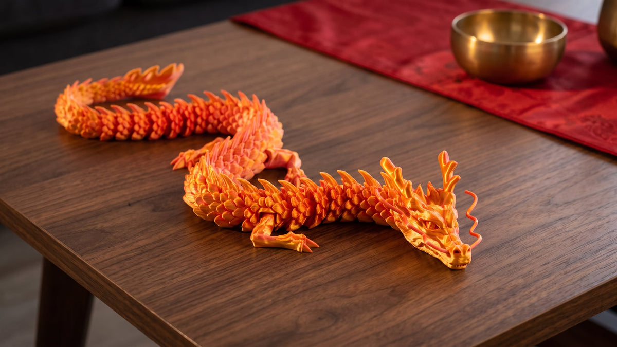 A red-gold 3D printed Chinese dragon with a long scaled body, four legs and antlers lying in an S-curve on a dark walnut table, a red runner and brass bowl behind it