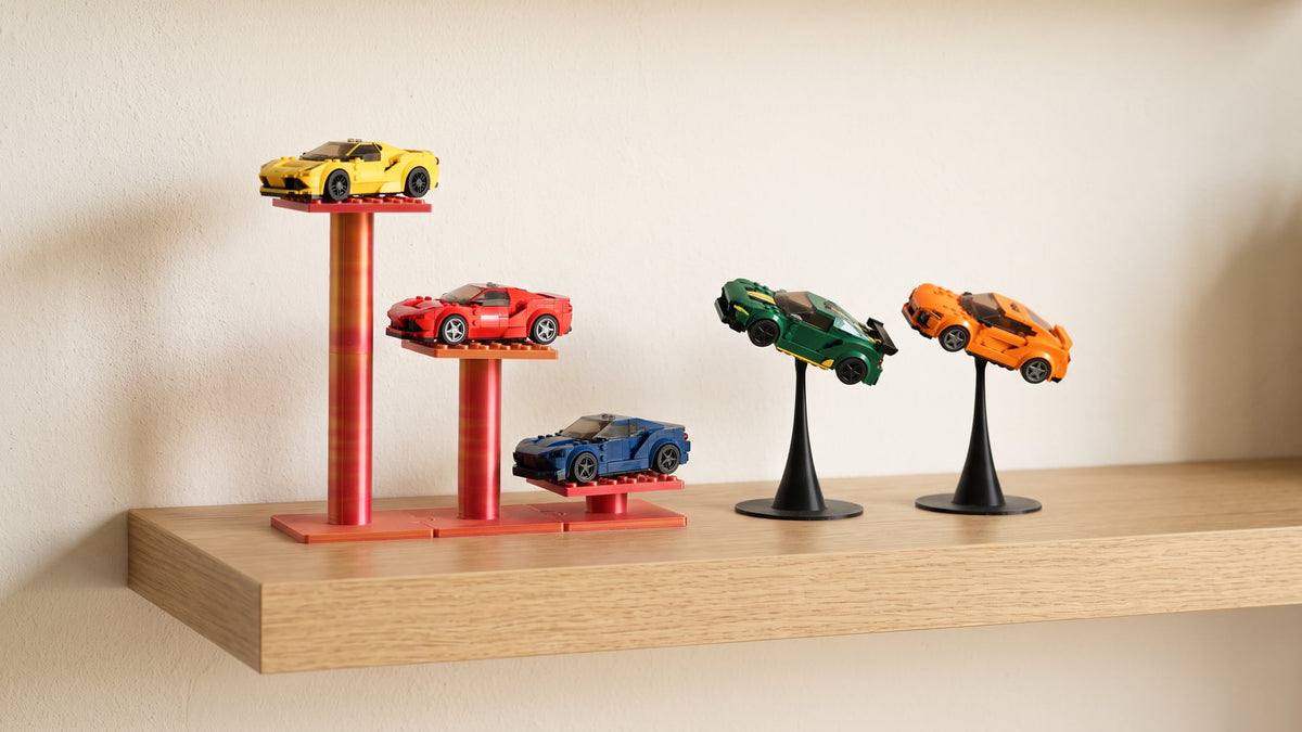 Wooden wall shelf with small brick-built sports cars on 3D printed stands: a red-gold three-level rack holding three cars at three heights and two black single stands holding cars tilted as if cornering